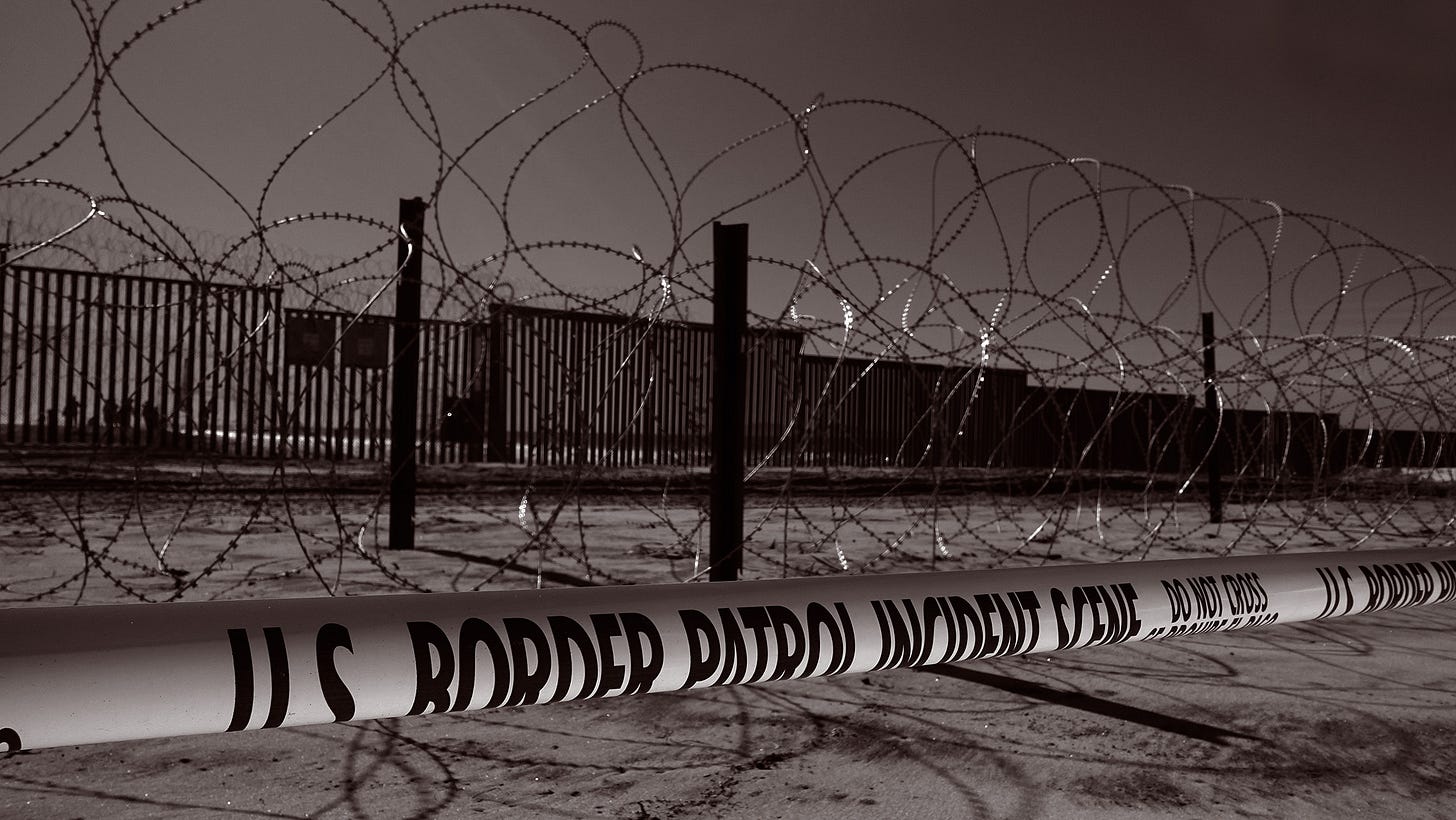 barbed wire in front of U.S. border wall, along with yellow police tape that says, "US Border Patrol incident scene'