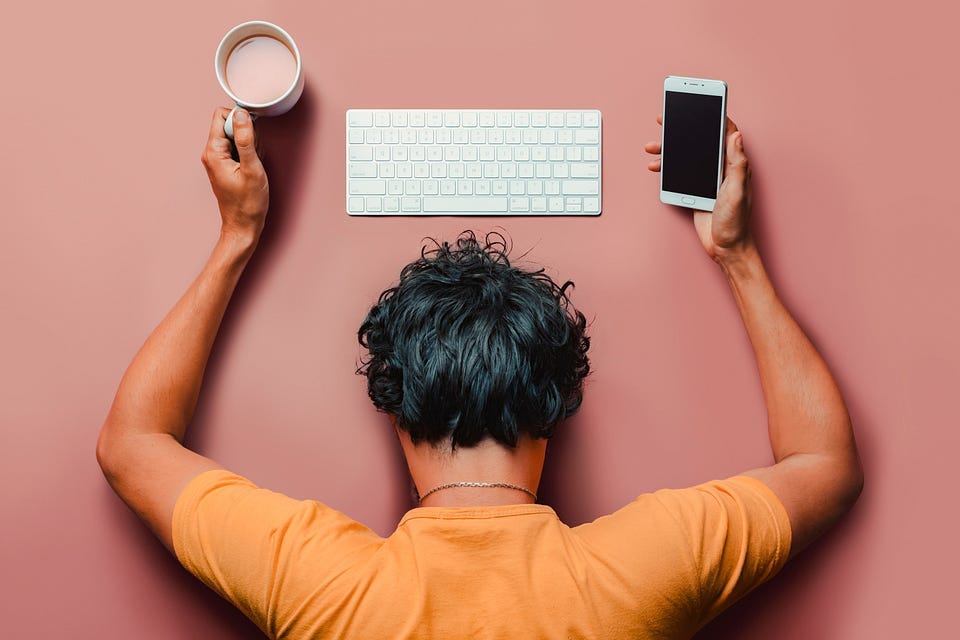 A person with a keyboard in front, a coffee mug in one hand and a smartphone in the other.