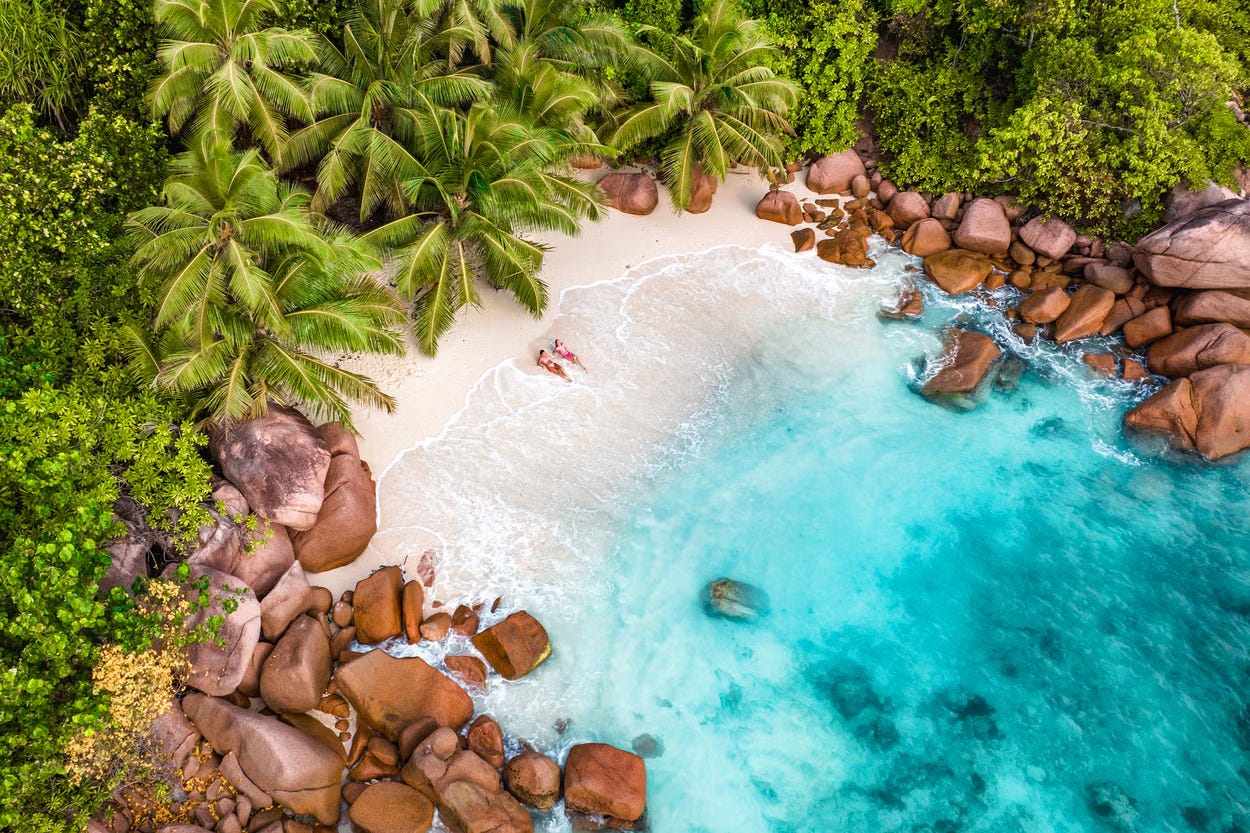 An overhead picture of a paradise beach, with golden sand, rocks, palms and a couple enjoying the sun An overhead picture of a paradise beach, with golden sand, rocks, palms and a couple enjoying the sun