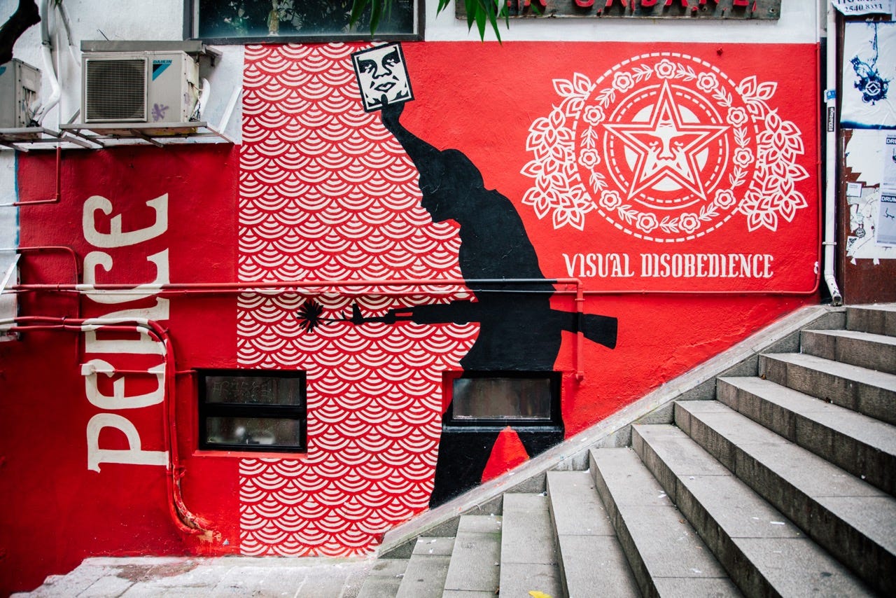 A red mural on a wall features a silhouette of a man holding a rifle and a sign with a face. Text A red mural on a wall features a silhouette of a man holding a rifle and a sign with a face. Text