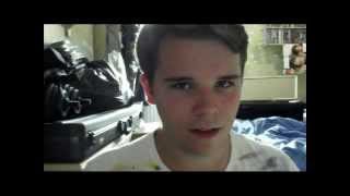 A clean-shaven baby-faced teenage boy sits in his bedroom looking to camera.