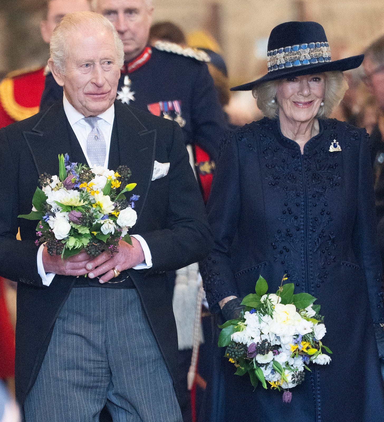 King Charles and Queen Camilla walking together holding flowers