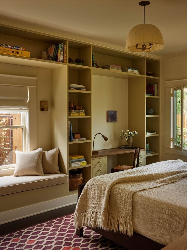 This may contain: a bed sitting in a bedroom under a window next to a book shelf filled with books