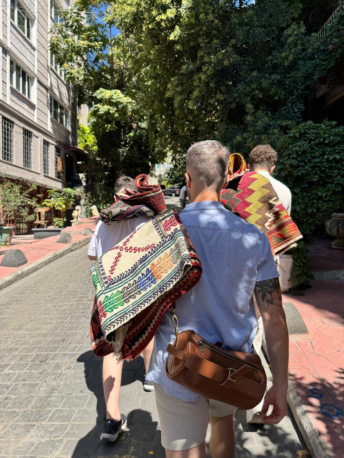 Back view of a man carrying a colorful Turkish rug over his shoulder while walking through the sunlit streets of Istanbul, symbolizing both the literal and figurative weight of transition