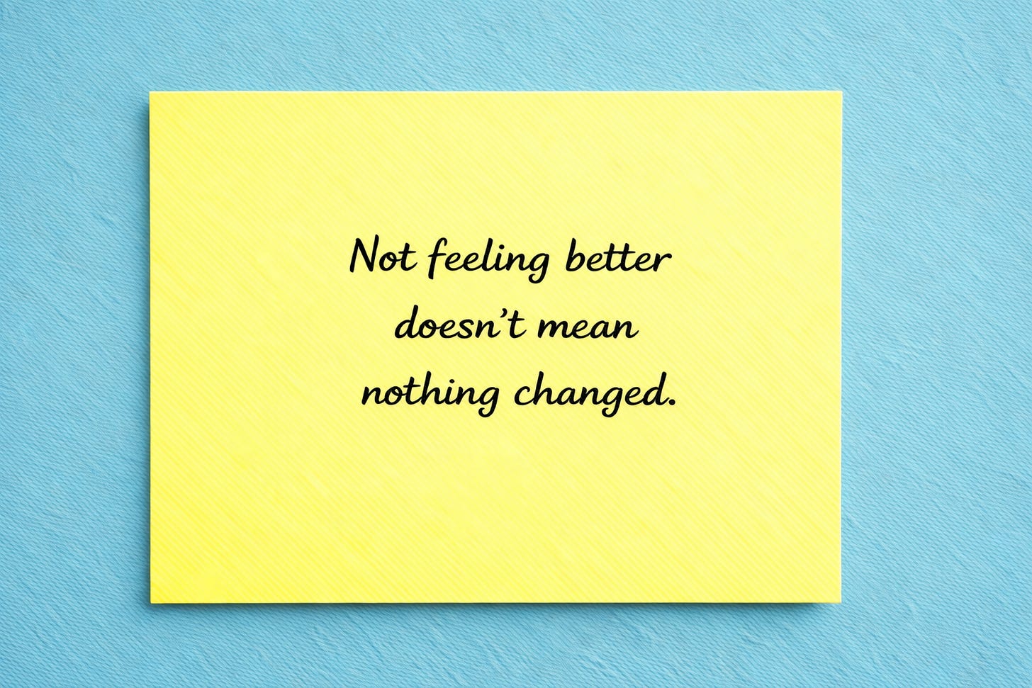 Yellow sticky note reading ‘Not feeling better doesn’t mean nothing changed’ on a soft blue background.