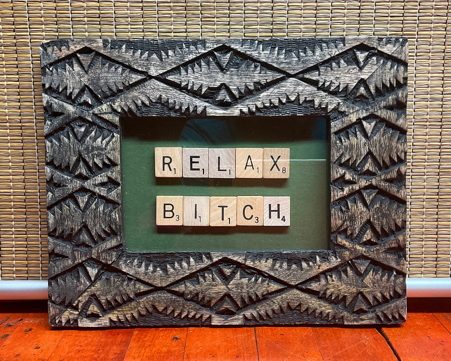 Carved rustic wood frame with scrabble tiles spelling out the words "Relax Bitch" on a green background.