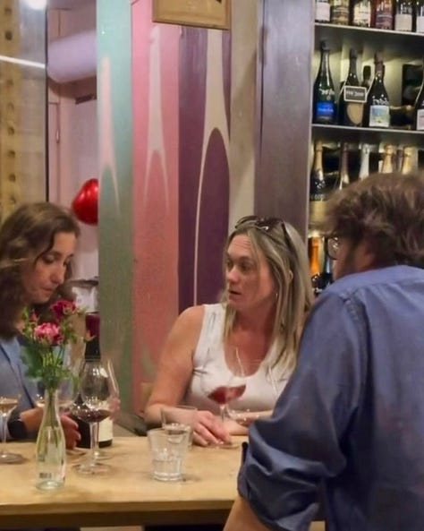 Photos inside In Vino wine bar in Yerevan, including a hand holding a bottle of Trinity Canyon Areni Noir, staff pouring wine behind shelves stocked with Armenian and international bottles, friends toasting with glasses of white wine, a long tasting table set with glassware beneath a sign reading 'The Renaissance of Armenian Wine Making,' and a wall of photos honoring winemakers