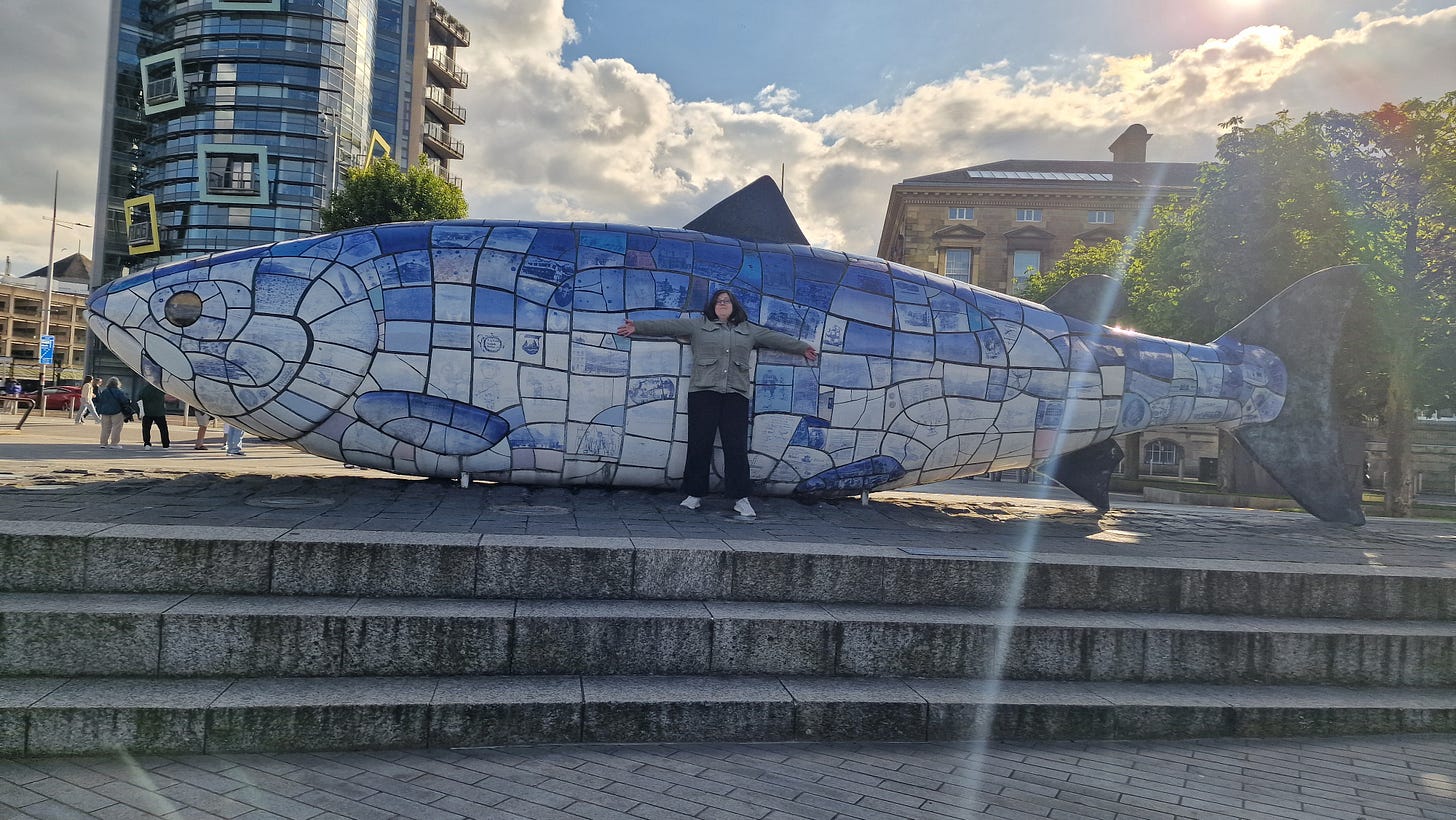 Photo of a massive, massive fish sculpture in Belfast. A person stands against it to show difference in scale (no pun intended).