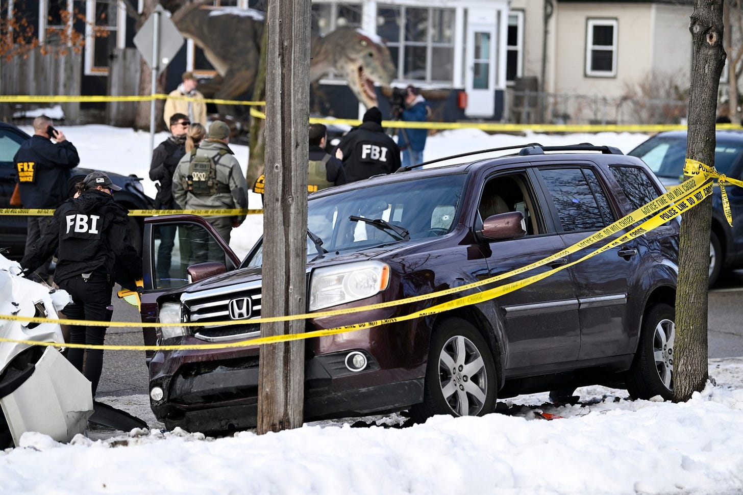FBI agents stand behind yellow police tape near a maroon SUV in the snow at an active investigation scene. FBI agents stand behind yellow police tape near a maroon SUV in the snow at an active investigation scene.