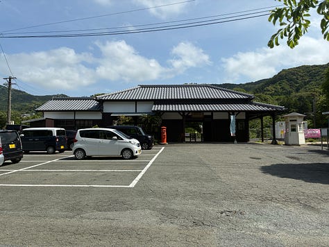 A rural Japanese train station, a signpost among leaves, orange orchards and cypress trees