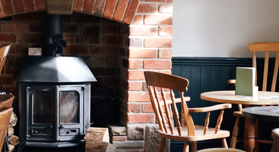 A pub with an iron fireplace with a brick arch, with a wooden table and chairs to the right of it