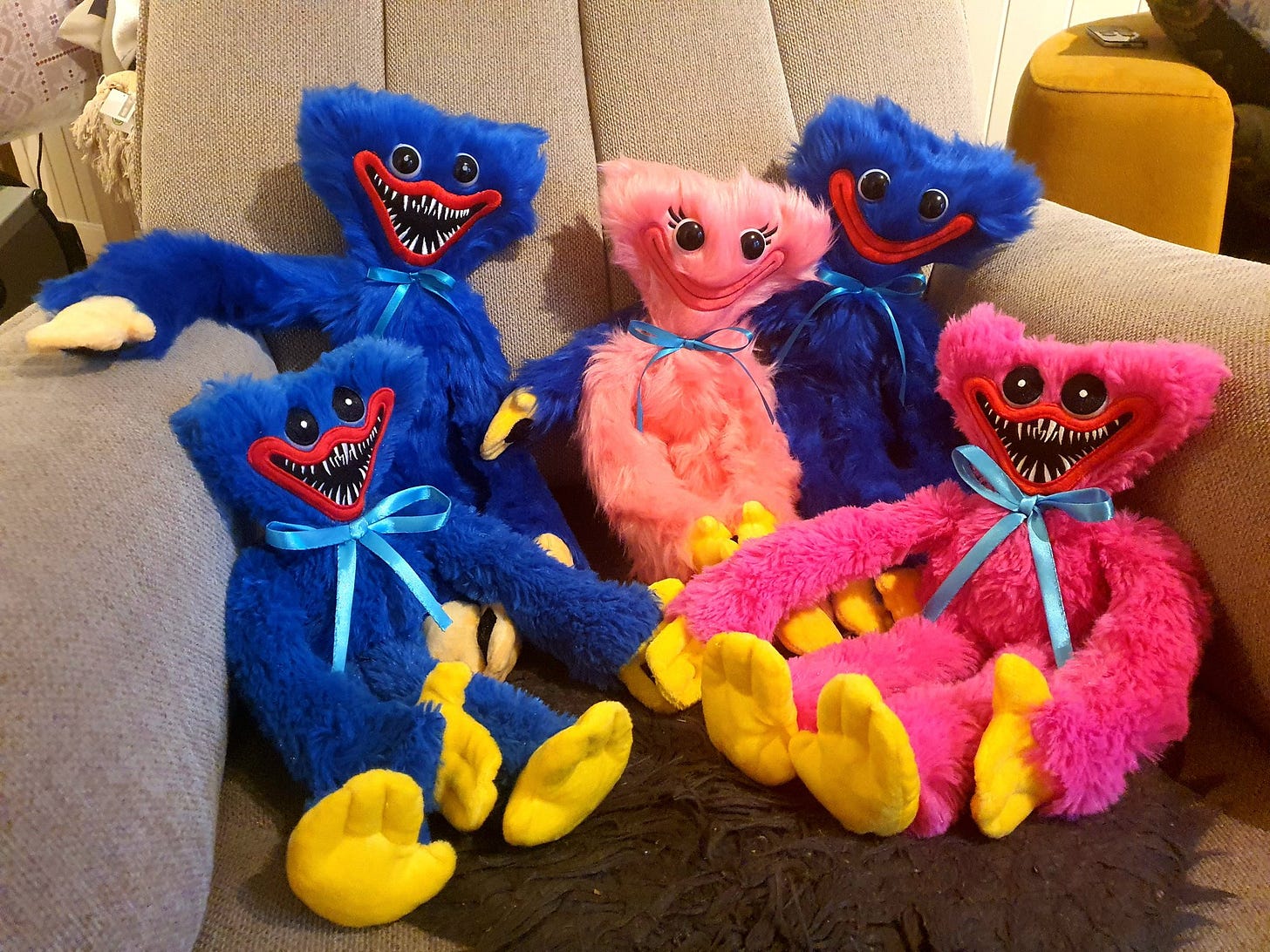 A variety of knockoff Huggy Wuggy plushies sitting on a taupe colored armchair. A variety of knockoff Huggy Wuggy plushies sitting on a taupe colored armchair.