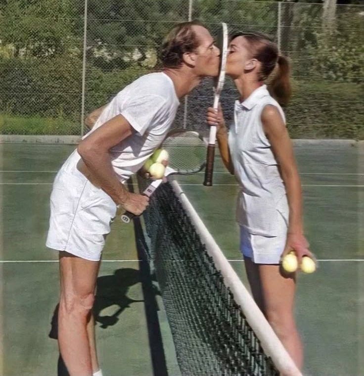 This may contain: two people standing on a tennis court with rackets and balls in their hands, kissing This may contain: two people standing on a tennis court with rackets and balls in their hands, kissing