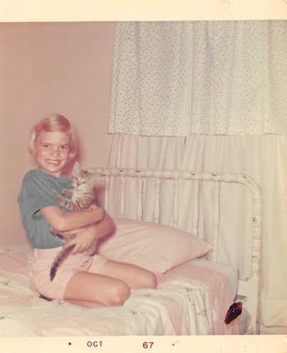 An old photograph of young Melora Fern sitting on a bed holding a small striped tabby