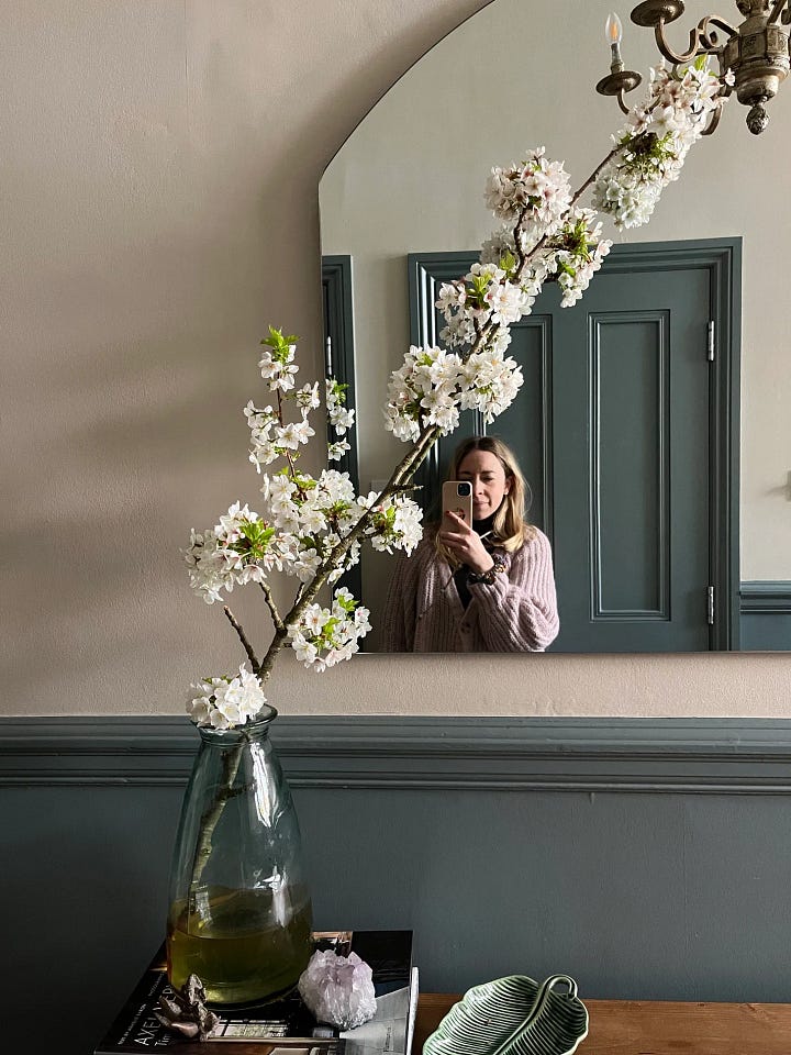 woman taking a photo of herself in mirror with blossom in front in a vase
