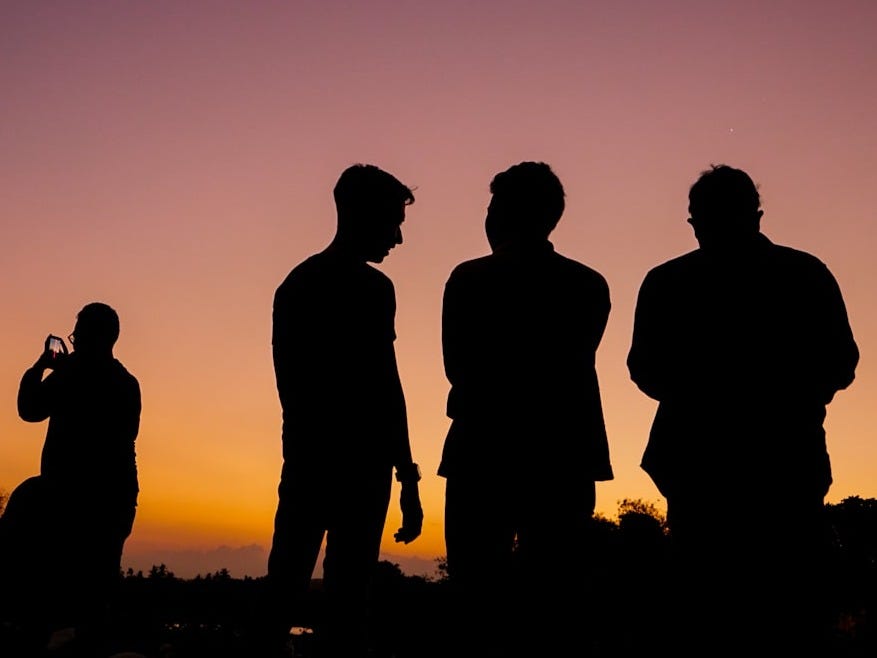 silhouette of 3 men standing on grass field during sunset