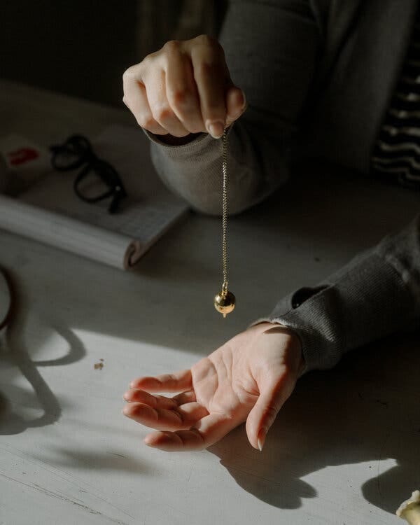 A picture of Helga Dörflinger’s hands holding a pendulum. A picture of Helga Dörflinger’s hands holding a pendulum.