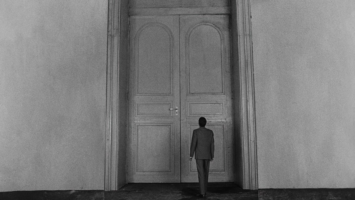 The Trial | Still features Anthony Perkins as Josef K against a massively sized door.
