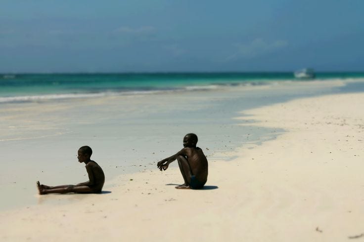 This may contain: two people sitting on the beach with their feet in the sand