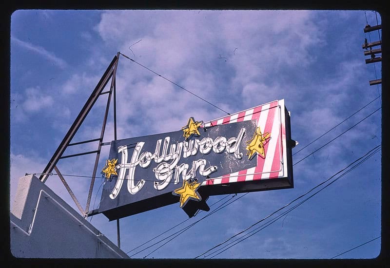 Color photograph of a hotel sign for "Hollywood Inn" with yellow stars and red and white stripes, hanging against a blue sky Color photograph of a hotel sign for "Hollywood Inn" with yellow stars and red and white stripes, hanging against a blue sky