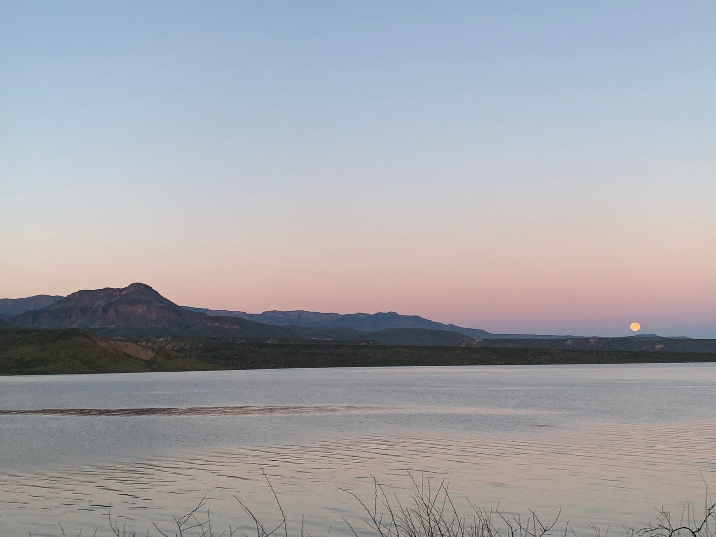 a lake with the sun setting over it in the distance, arizona rocky mountains in the distance at dusk. 