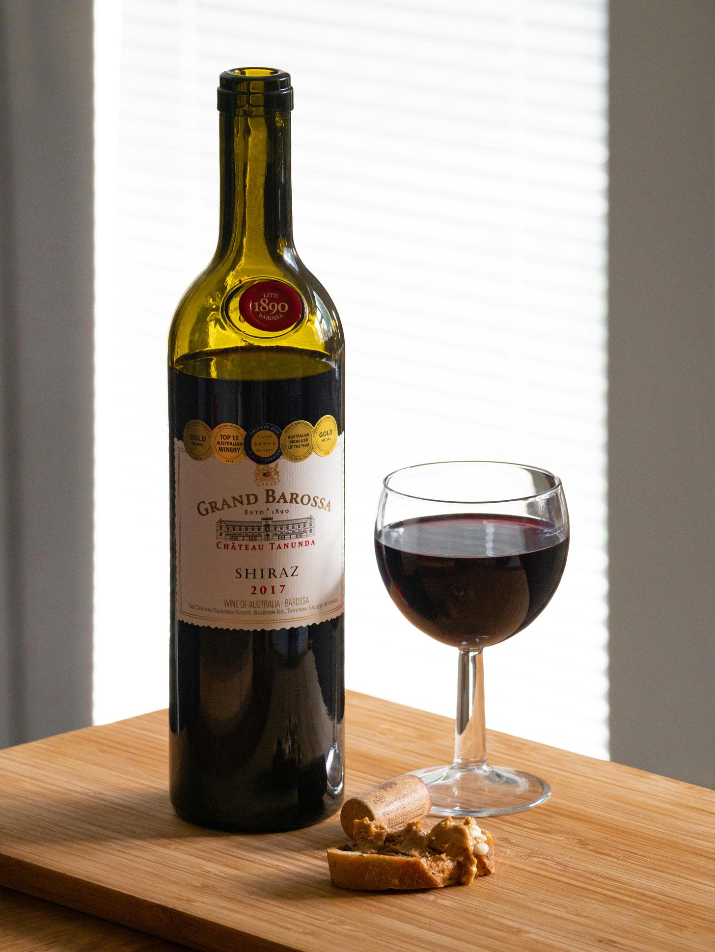 A bottle of wine and a glass of red wine on a cutting board.