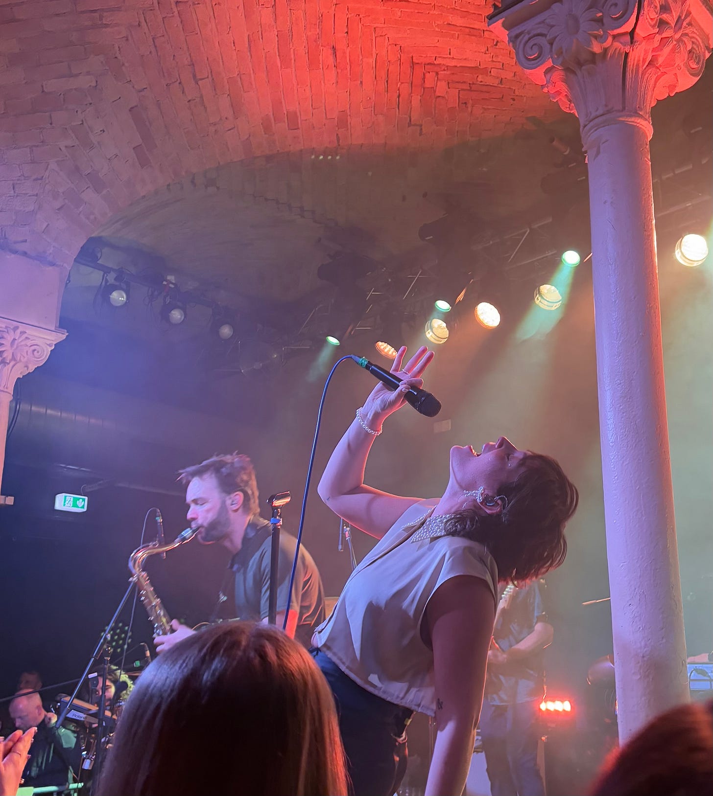 Sammy Rae from Sammy Rae & The Friends leaning back, singing into a microphone with her saxophonist in the background