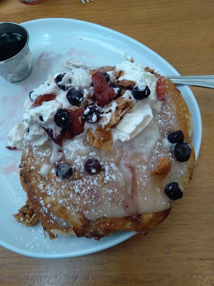 A plate of pancakes messily covered with berries, almond brittle and cream, and whipped cream. A plate of pancakes messily covered with berries, almond brittle and cream, and whipped cream.
