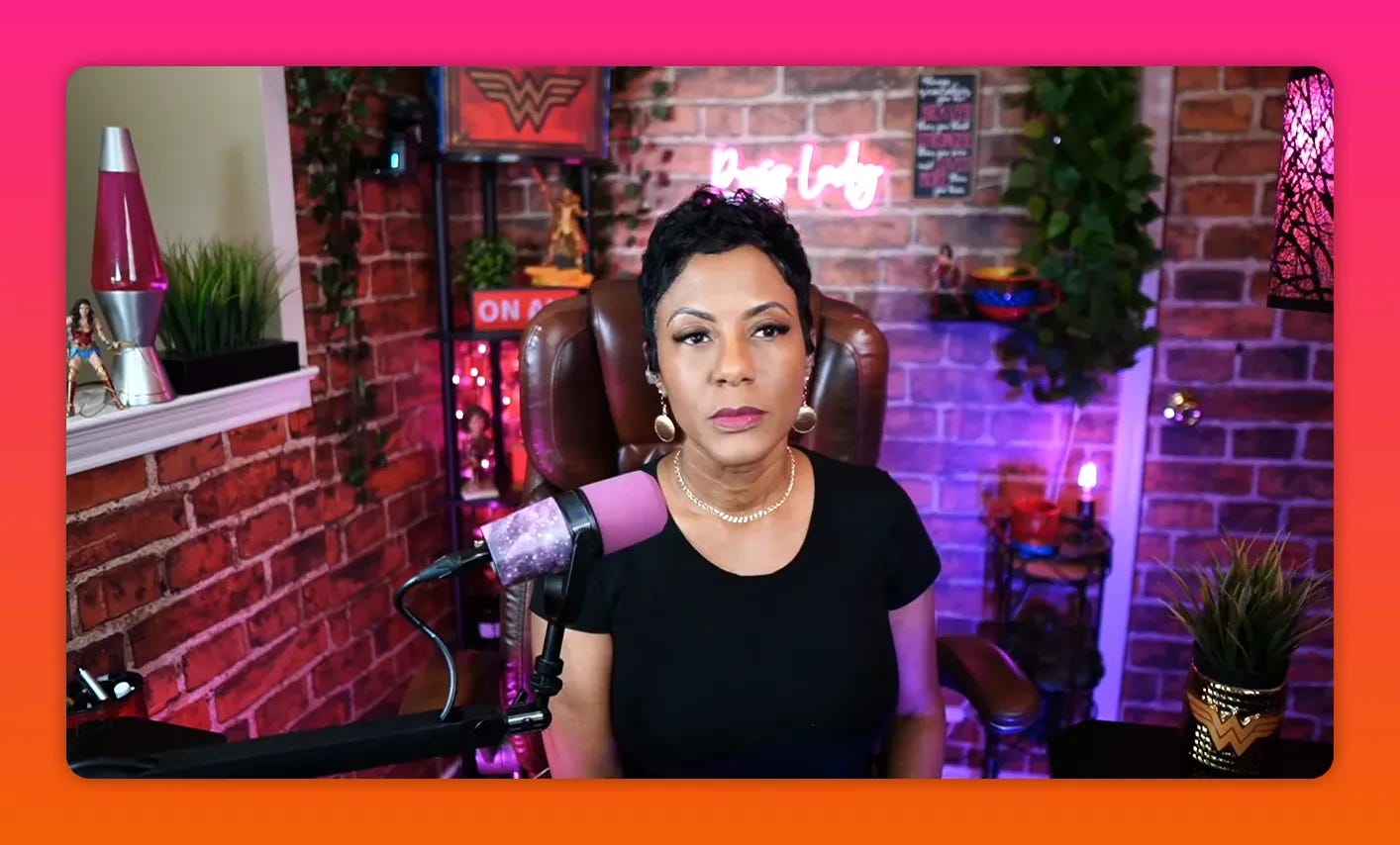Front-facing mid shot of presenter with pink microphone, brick wall backdrop and colored accent lighting
