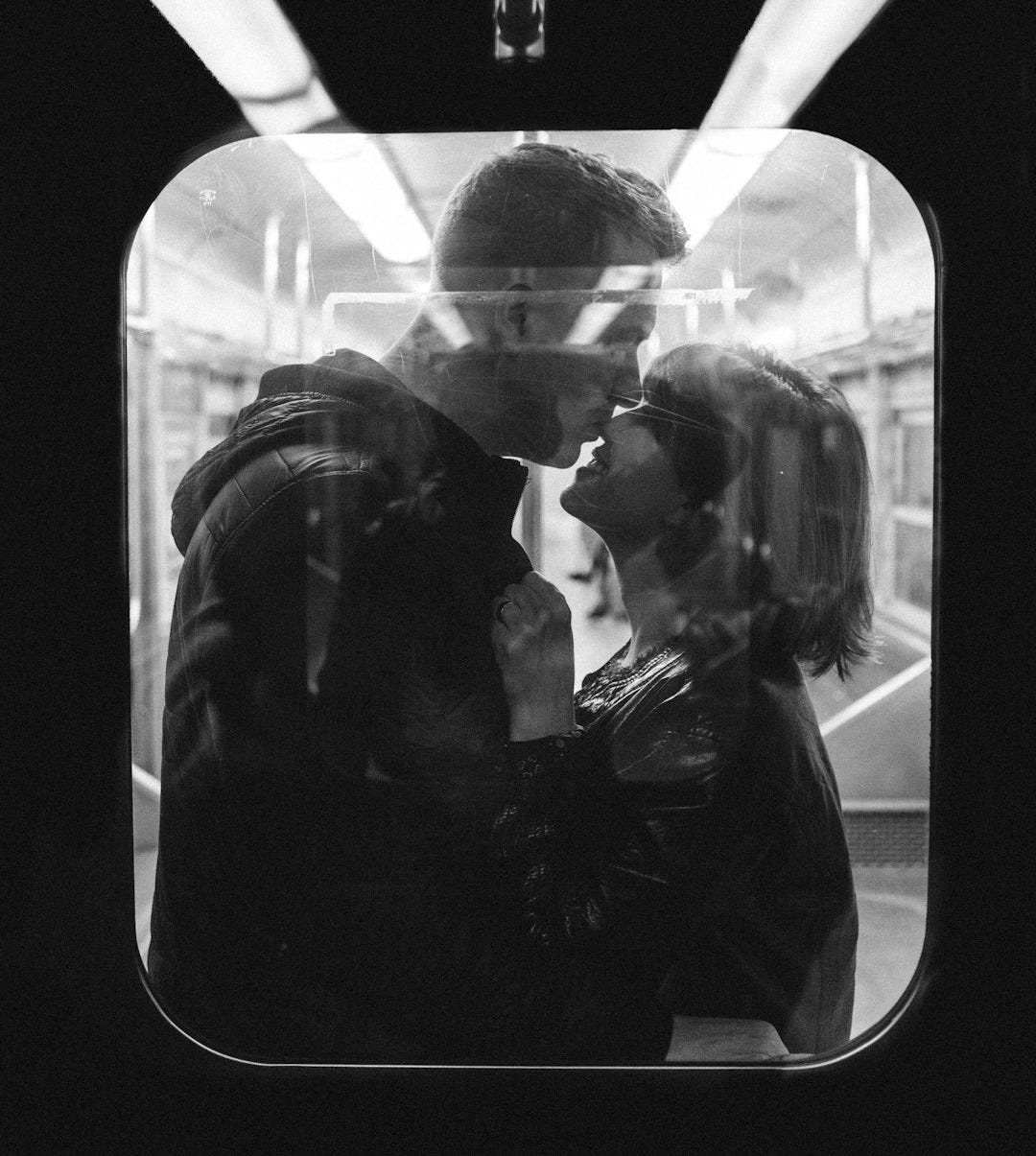 couple standing on window in grayscale photography