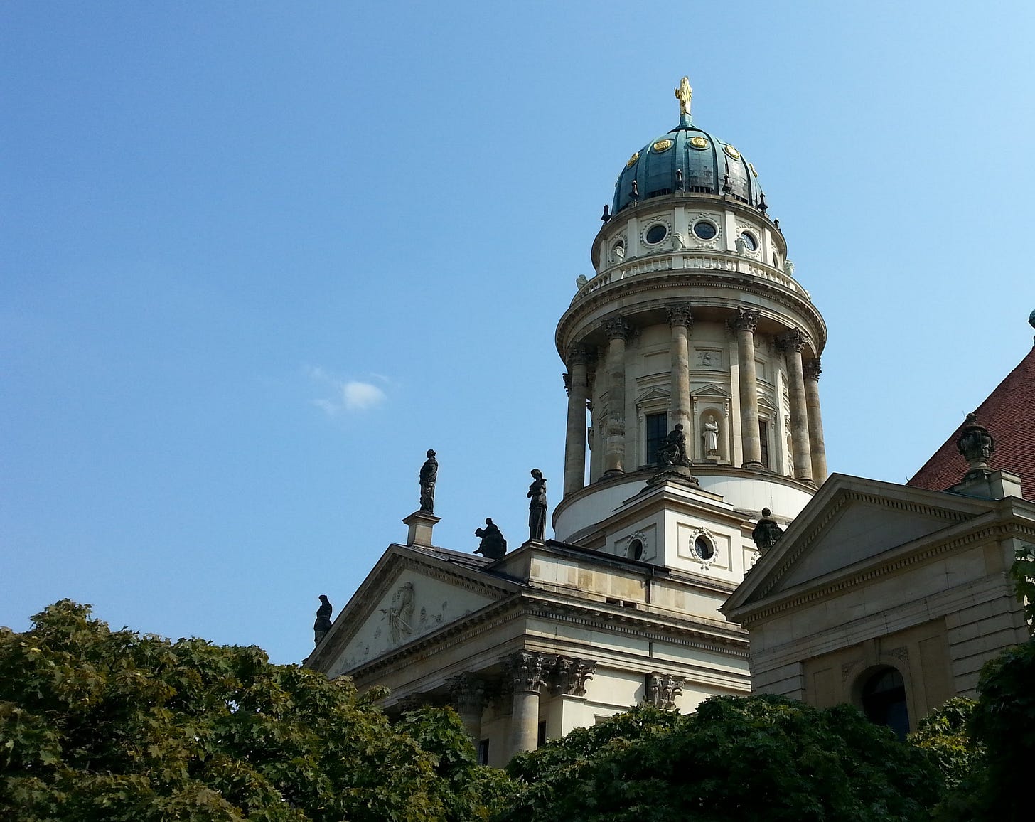Cupola di una chiesa neoclassica, con colonne e statue. Si staglia contro un cielo azzurrissimo. In basso, cime di alberi.