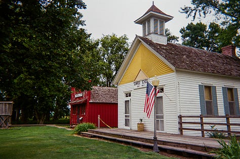 Red train engine with caboose. | An old typewriter used to relay messages to passing trains. | A white and yellow schoolhouse with an American flag.