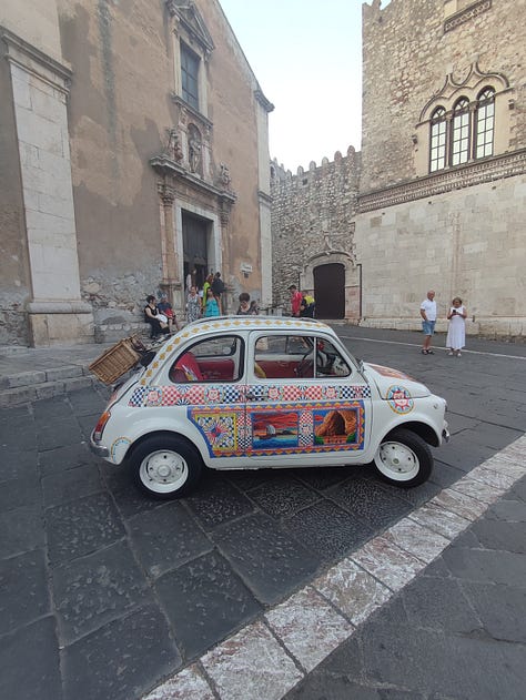 View of Mount Etna, misty in the distance from the Greek Theatre, Taormina; a tub of vegan chocolate gelato, Taormina, bubble car with colourful traditional Sicilian decoration parked in front of a church in Taormina, Sicily