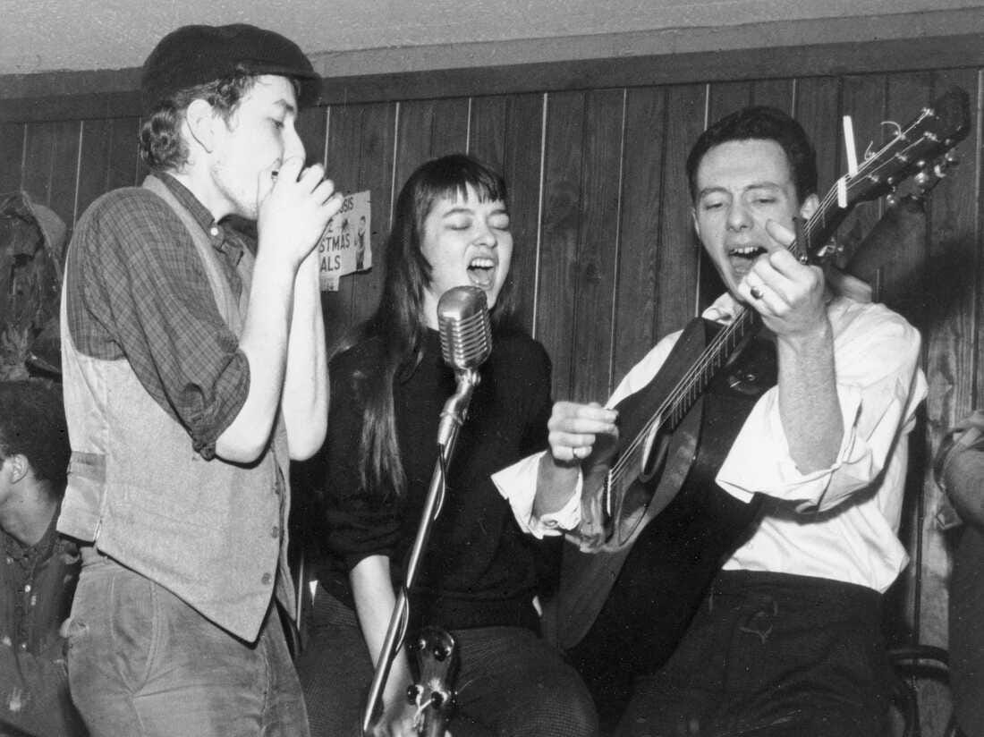 Karen Dalton (center) performing with Bob Dylan (left) & Fred Neil (right). Dalton is singing, Dylan is playing harmonica, and Neil is playing guitar.