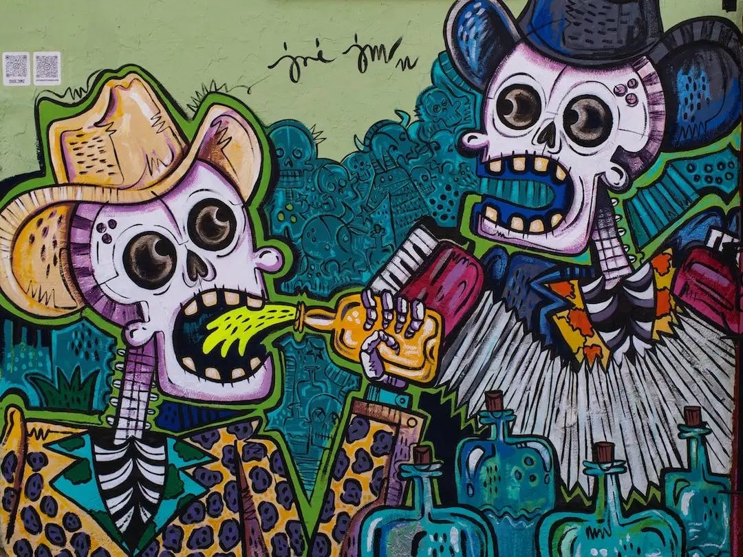 Street art - two human skeletons wearing stetsons, one drinking tequila from a bottle, the other playing an acordion