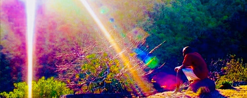 A man sitting on a stone with his back to the viewer, colorful beams shining down on him