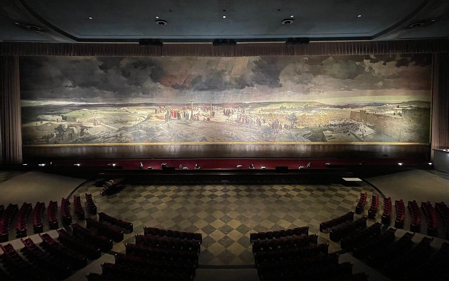 A darkened auditorium facing an immense painted panorama: a crowd gathers on a rocky hill around Christ standing before the cross, with the walls of Jerusalem in the distance. A darkened auditorium facing an immense painted panorama: a crowd gathers on a rocky hill around Christ standing before the cross, with the walls of Jerusalem in the distance.