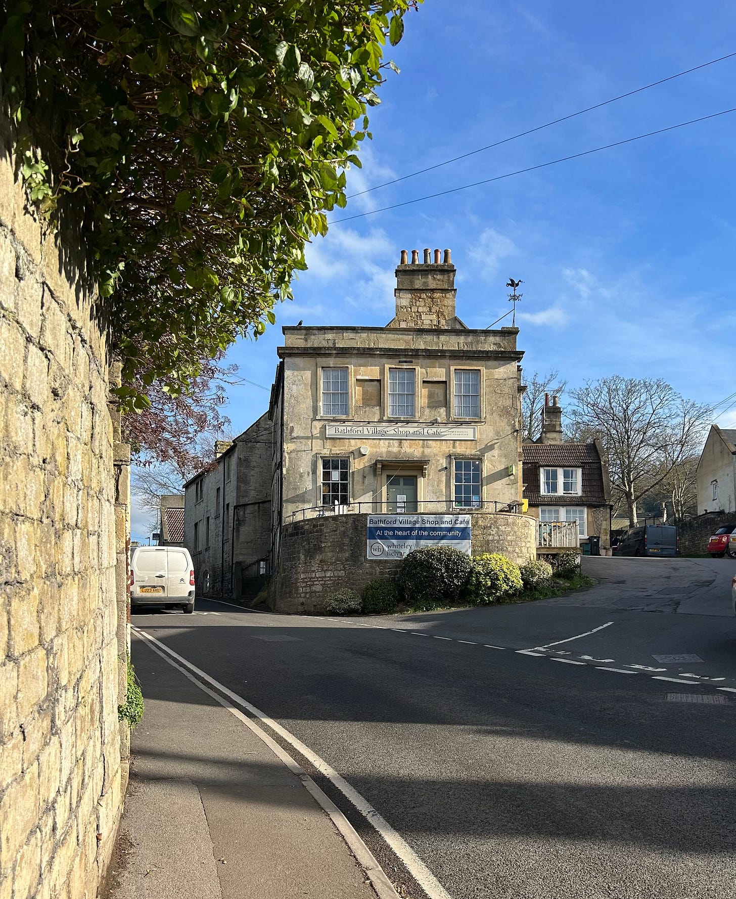 The Bathford Village shop on the corner of two roads, one to the left, the other to the right. The sky is blue. The Bathford Village shop on the corner of two roads, one to the left, the other to the right. The sky is blue.