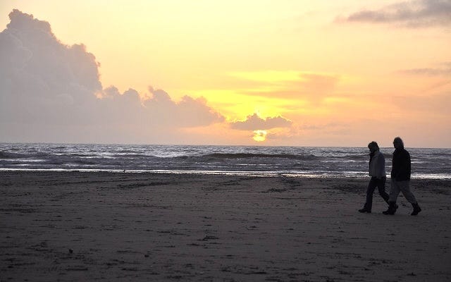 silhouettes of two walkers on beach at sunset silhouettes of two walkers on beach at sunset