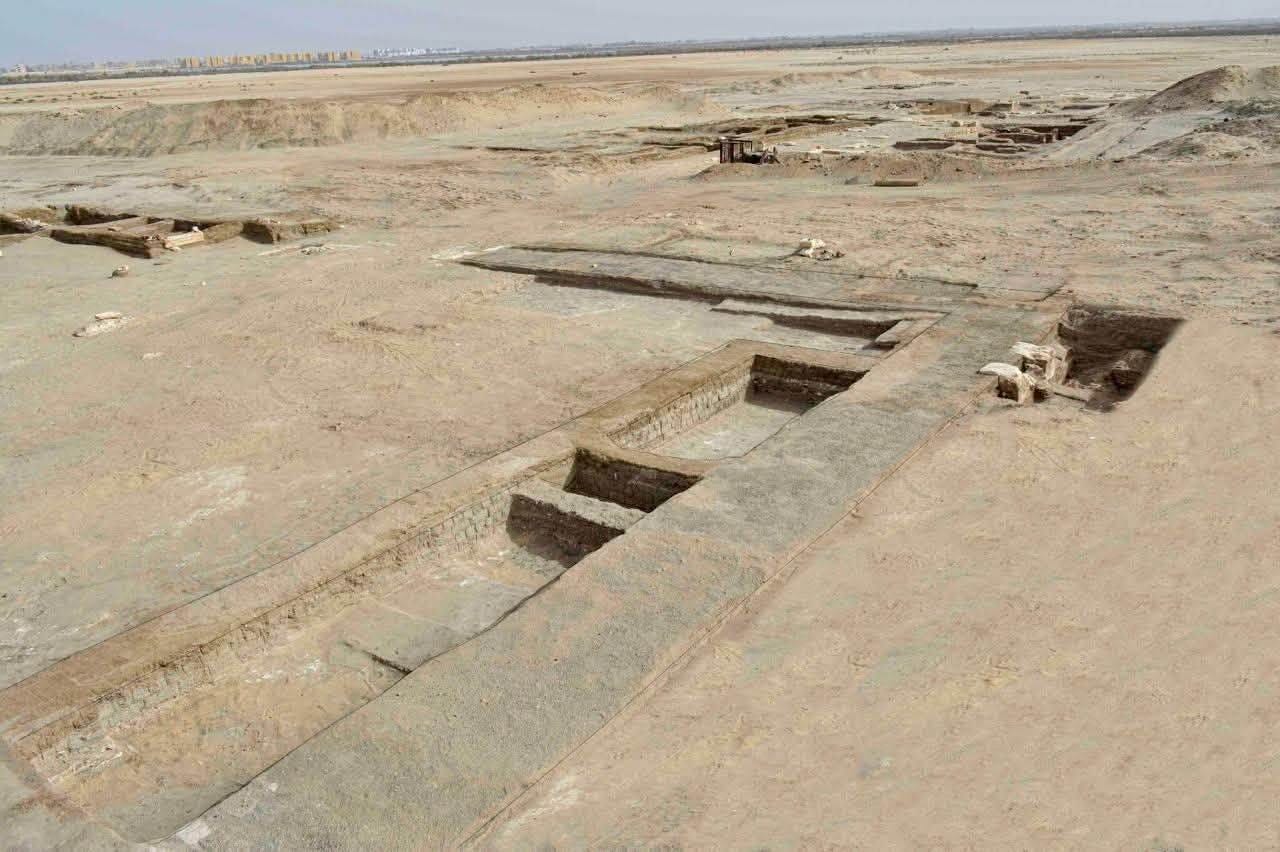Excavation along a mudbrick wall at Tell el-Kharouba, running diagonally across the site with further structures cleared beyond it.