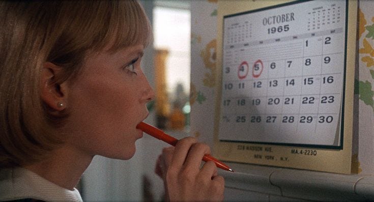 This may contain: a woman is holding a pencil in her mouth and looking at a calendar on the wall