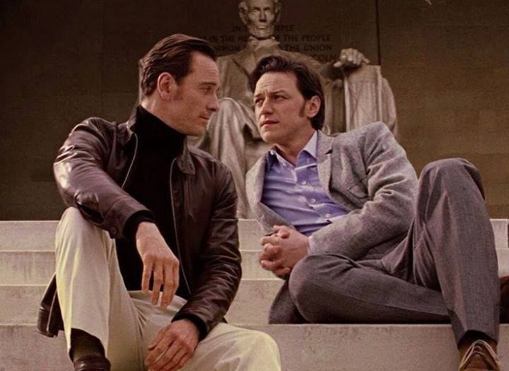 This may contain: two men sitting on the steps talking to each other in front of a fountain with statues behind them