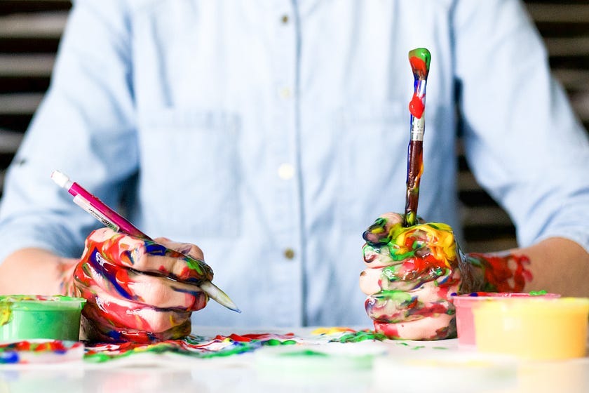 A man in a dress shirt, holding a marker and a paint brush with colorful paint blobs covering his hands and arms — indicating creative thinking A man in a dress shirt, holding a marker and a paint brush with colorful paint blobs covering his hands and arms — indicating creative thinking