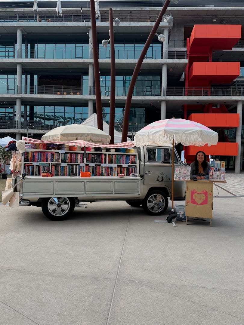 The Fleuria's bookmobile full of books outside of a large glass building The Fleuria's bookmobile full of books outside of a large glass building