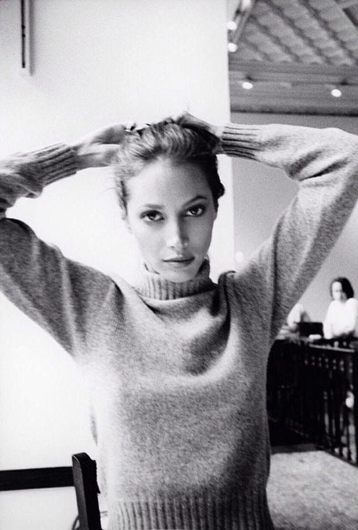 This may contain: a black and white photo of a woman with her hands on her head wearing a turtle neck sweater