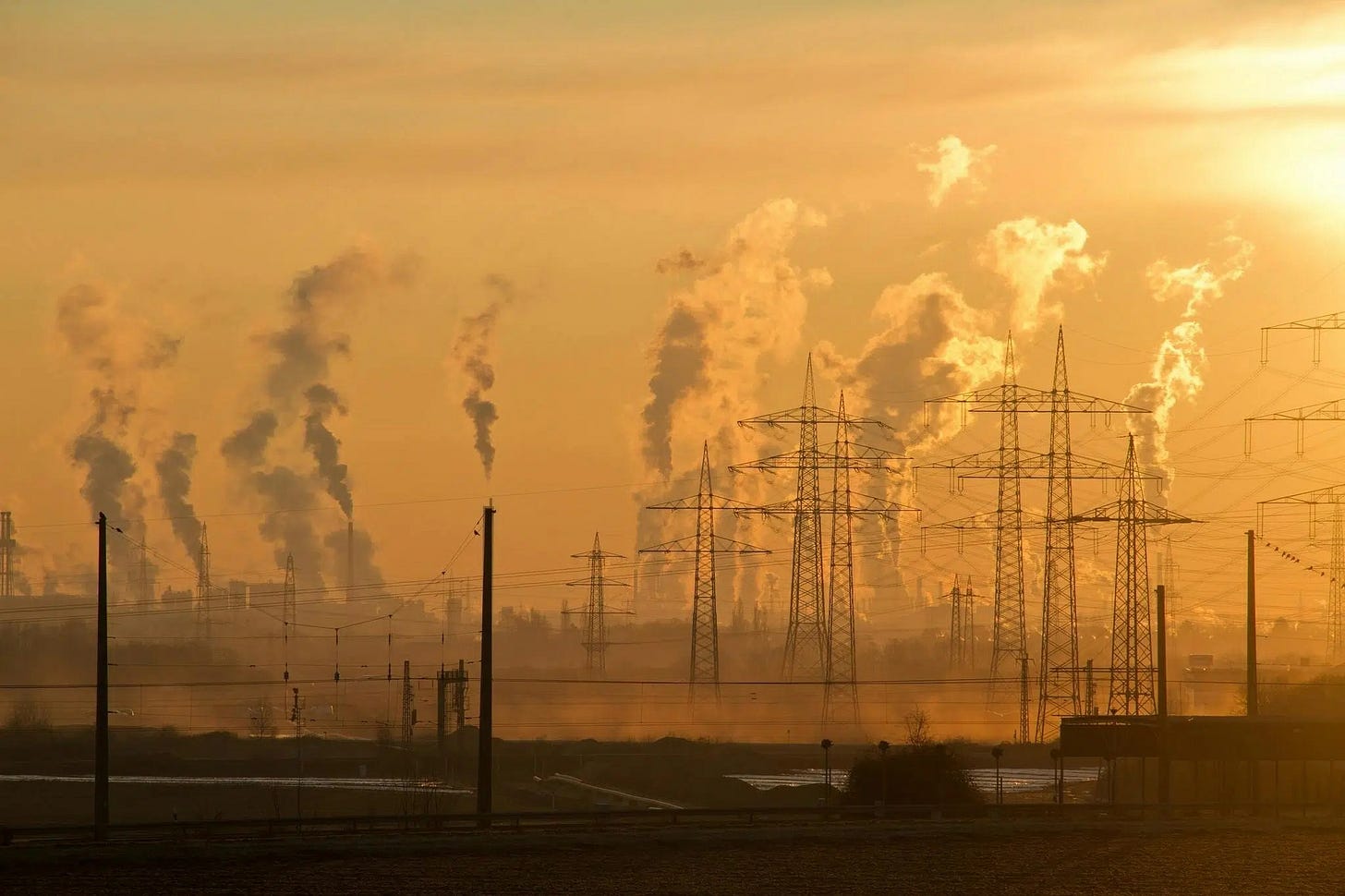 An image of smokestacks and electric towers during sunset.