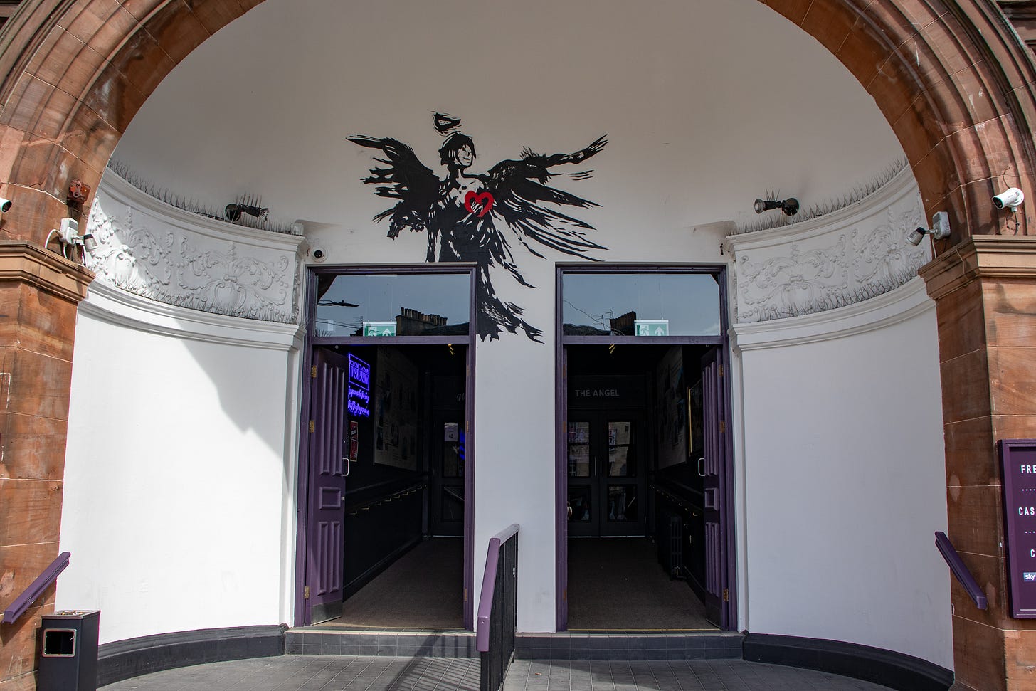 A large brick archway with two purple doors in it, and a large illustration of an angel above.