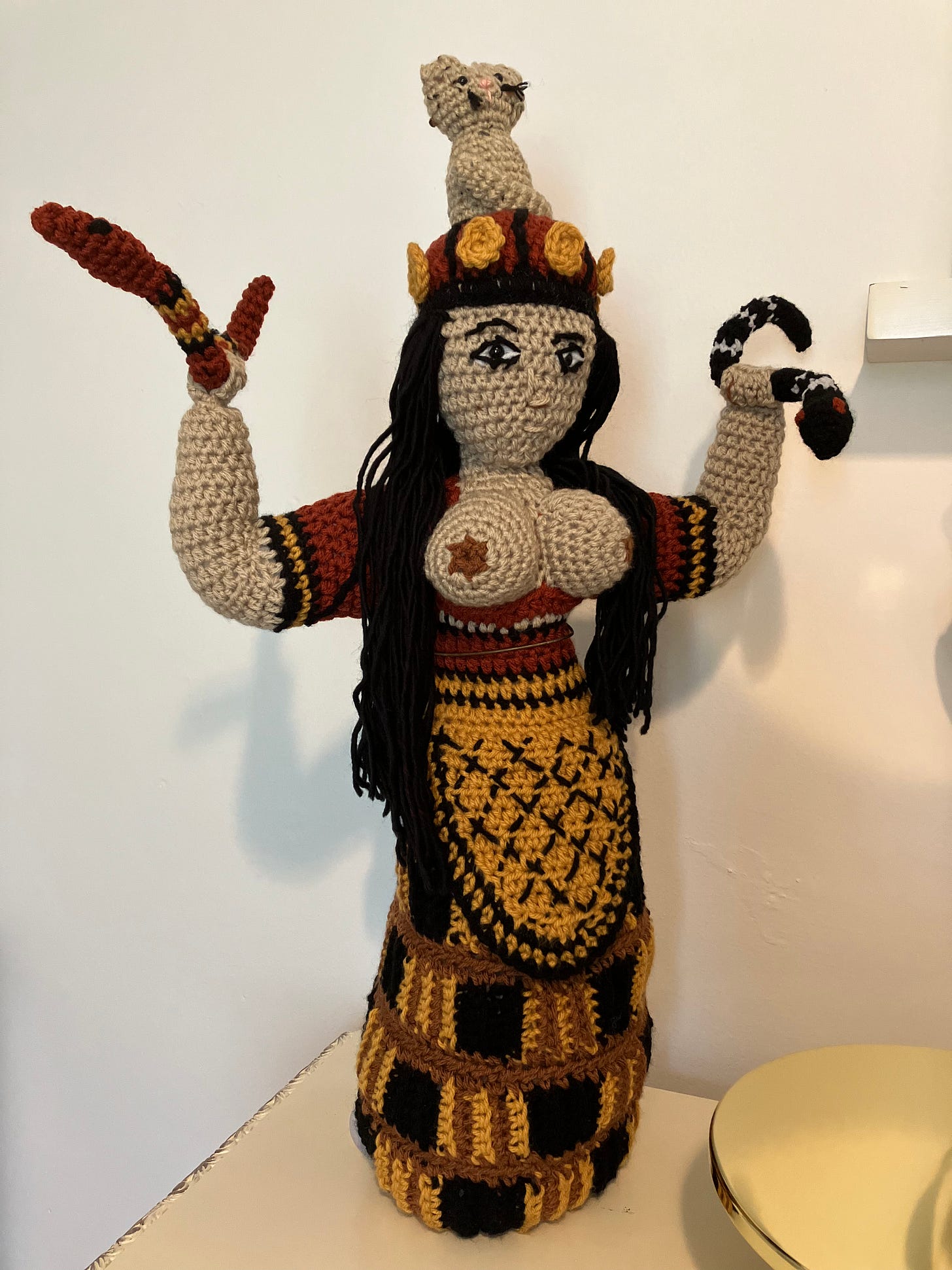 Giant hand-crocheted Snake Goddess figurine in the same colors as the original, with drapey yarn hair and a snake in each hand.