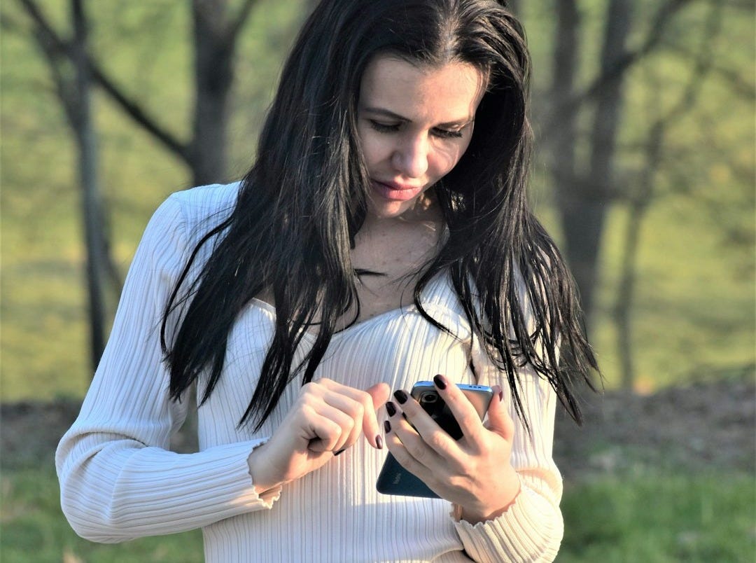 a woman in a white shirt is looking at her cell phone