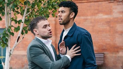 One teacher holds another back as he looks toward something off screen